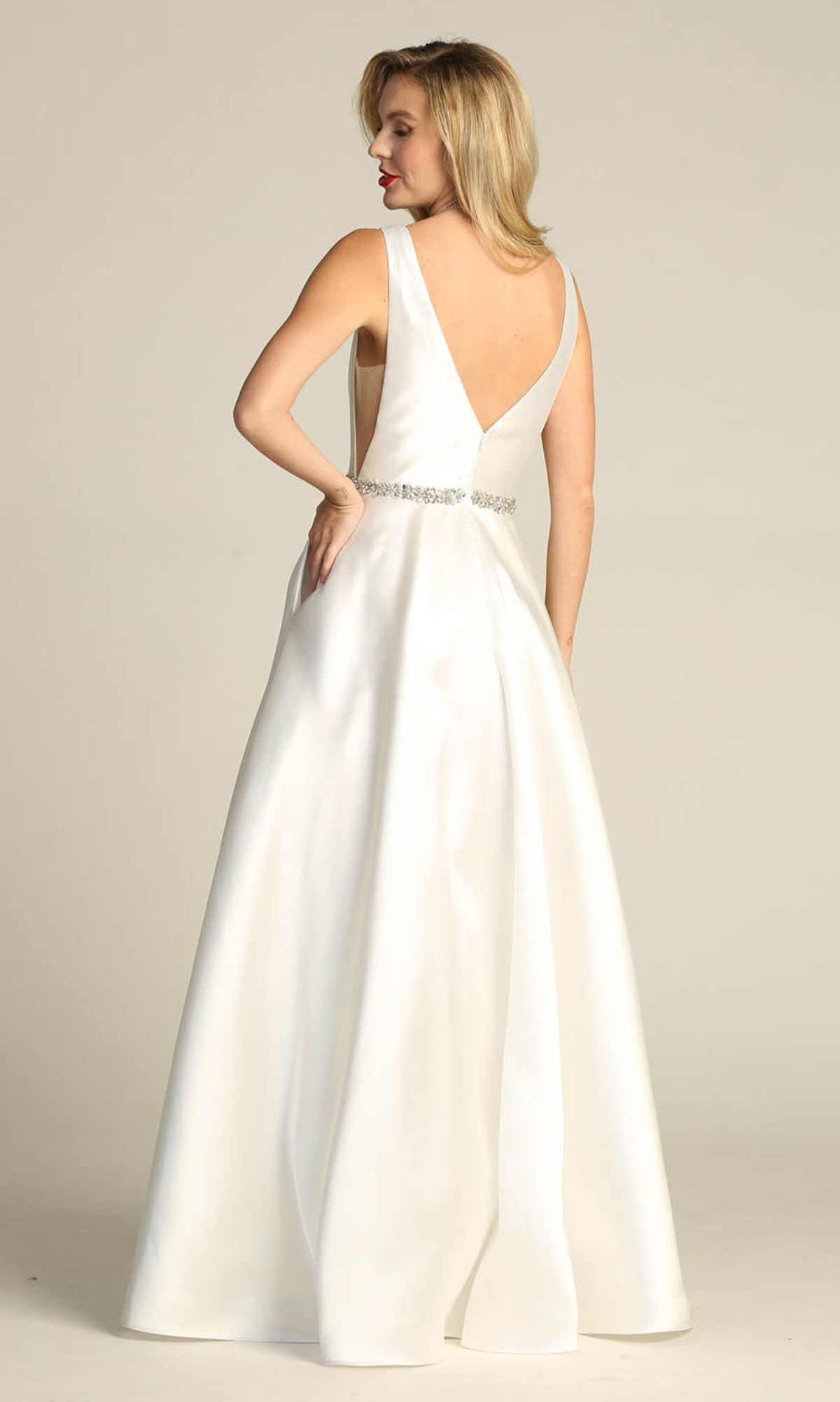A woman in the Chicas CC3021 Jeweled-Waist Long Prom Ball Gown, featuring a sleeveless A-line design and deep V-back, stands looking over her shoulder against a plain background.